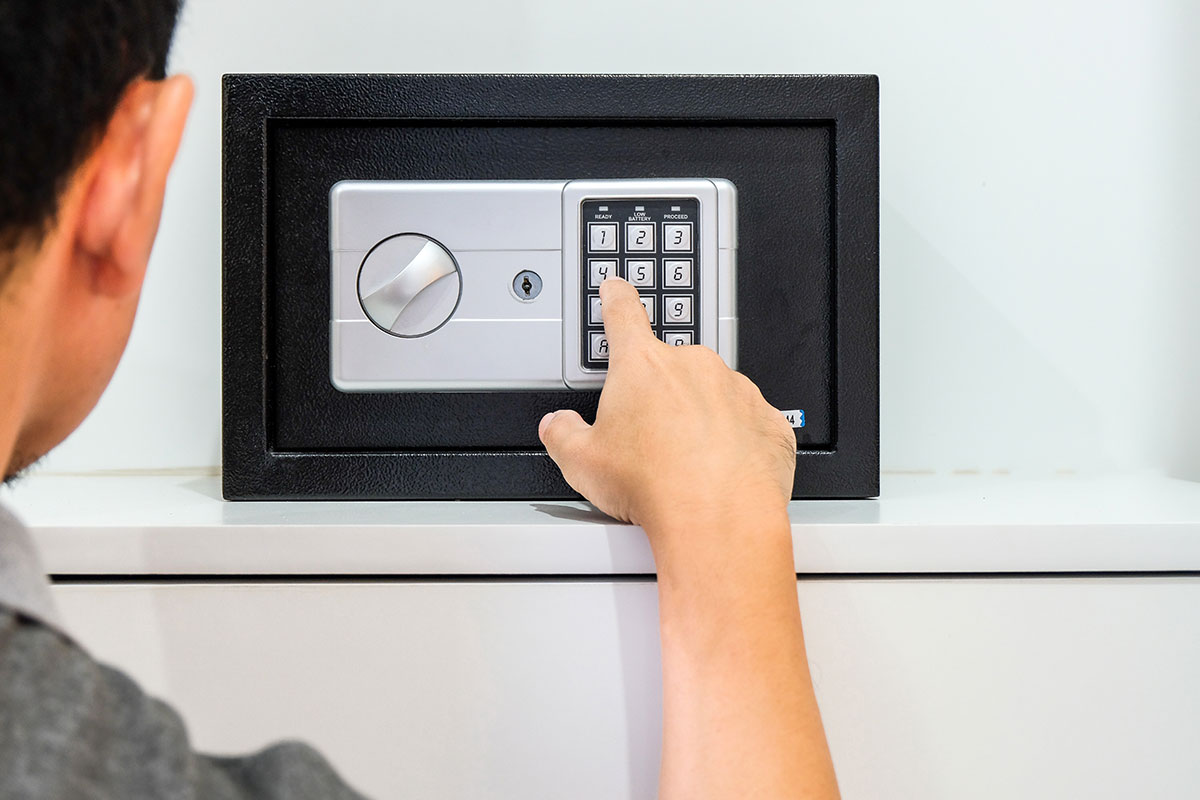 A person is entering a code on the digital keypad of a home safe mounted on the wall.